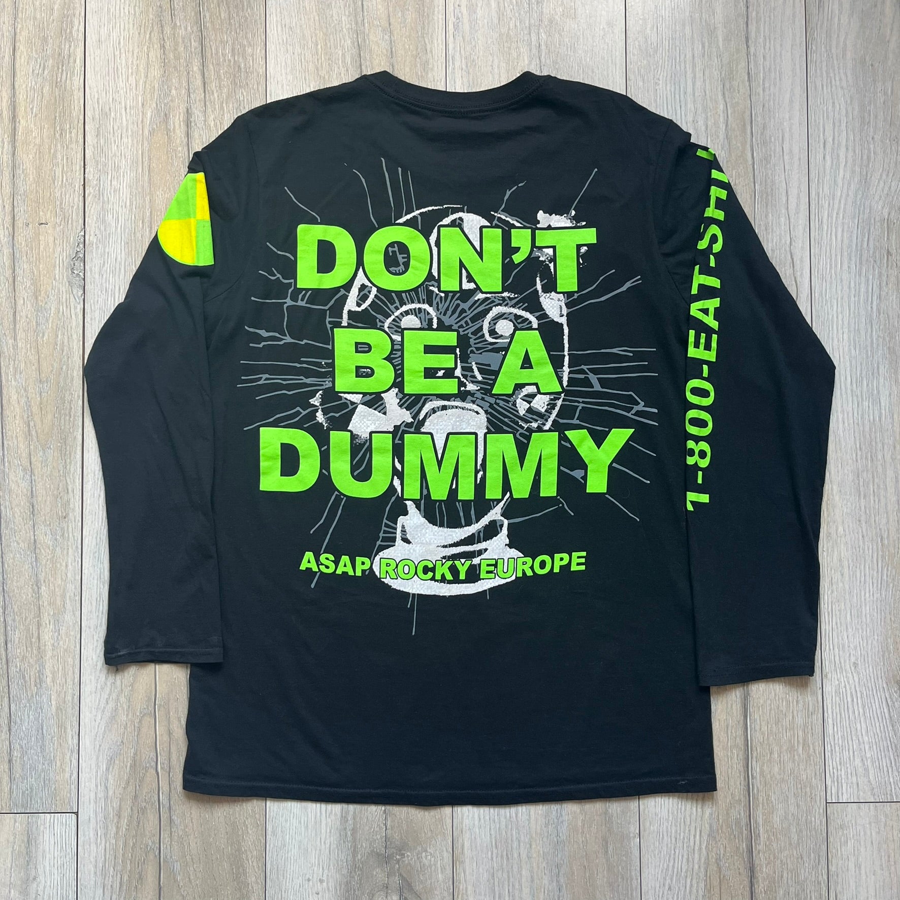 A$AP Rocky 2019 “Injured Generation” Tour “Pickpockets” Longsleeve is a black long-sleeve T-shirt released as part of the Injured Generation tour merchandise collection. The front features a large graphic of A$AP Rocky with green “Warning! Beware of Pickpockets” text. One sleeve includes “1-800-EAT-SHIT” text, while the other features a yellow and green testing-style logo. The back displays large green “Don’t Be a Dummy A$AP Rocky Europe” text layered over a white dummy mask graphic. Made in the USA.