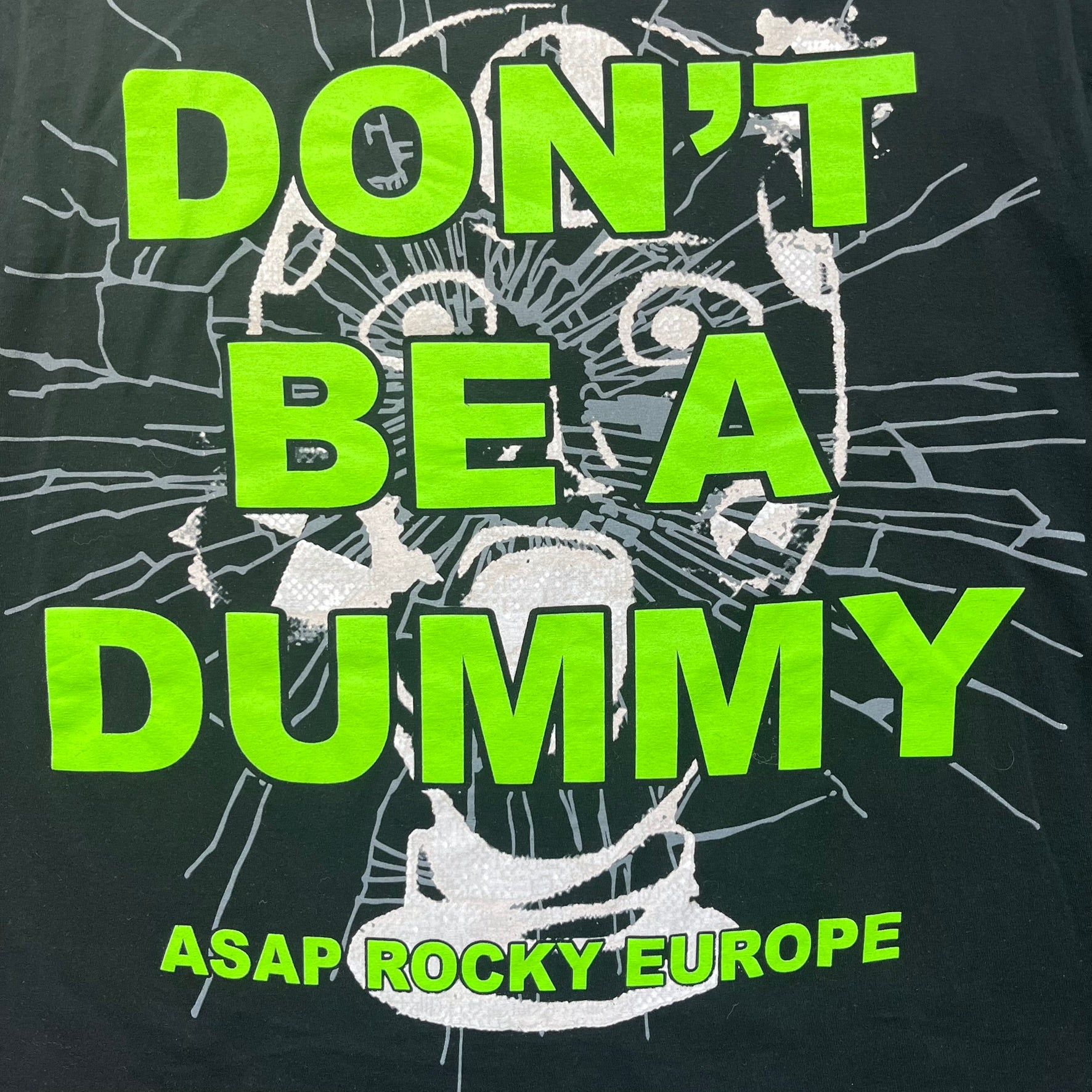 A$AP Rocky 2019 “Injured Generation” Tour “Pickpockets” Longsleeve is a black long-sleeve T-shirt released as part of the Injured Generation tour merchandise collection. The front features a large graphic of A$AP Rocky with green “Warning! Beware of Pickpockets” text. One sleeve includes “1-800-EAT-SHIT” text, while the other features a yellow and green testing-style logo. The back displays large green “Don’t Be a Dummy A$AP Rocky Europe” text layered over a white dummy mask graphic. Made in the USA.
