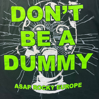 A$AP Rocky 2019 “Injured Generation” Tour “Pickpockets” Longsleeve is a black long-sleeve T-shirt released as part of the Injured Generation tour merchandise collection. The front features a large graphic of A$AP Rocky with green “Warning! Beware of Pickpockets” text. One sleeve includes “1-800-EAT-SHIT” text, while the other features a yellow and green testing-style logo. The back displays large green “Don’t Be a Dummy A$AP Rocky Europe” text layered over a white dummy mask graphic. Made in the USA.