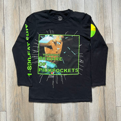 A$AP Rocky 2019 “Injured Generation” Tour “Pickpockets” Longsleeve is a black long-sleeve T-shirt released as part of the Injured Generation tour merchandise collection. The front features a large graphic of A$AP Rocky with green “Warning! Beware of Pickpockets” text. One sleeve includes “1-800-EAT-SHIT” text, while the other features a yellow and green testing-style logo. The back displays large green “Don’t Be a Dummy A$AP Rocky Europe” text layered over a white dummy mask graphic. Made in the USA.