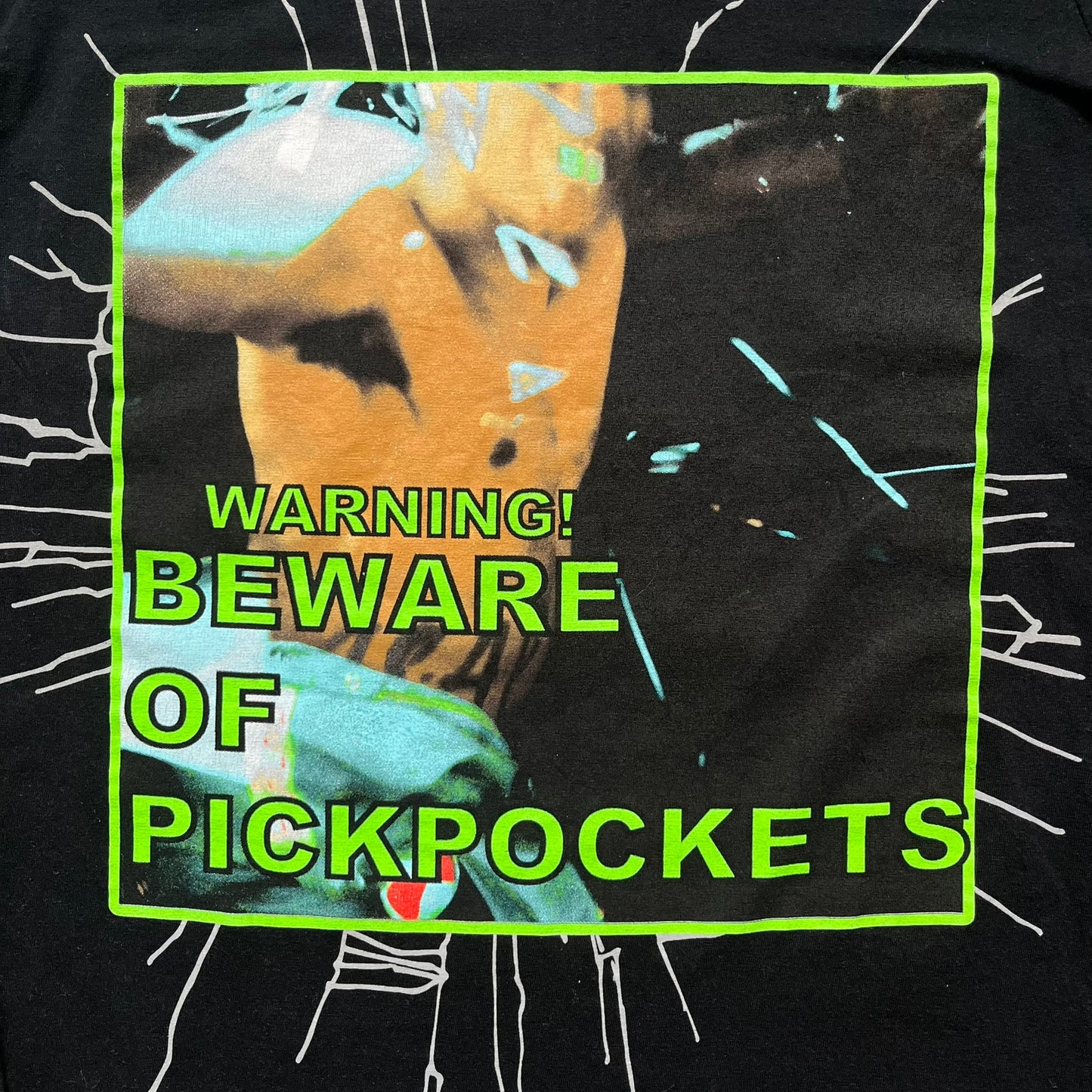 A$AP Rocky 2019 “Injured Generation” Tour “Pickpockets” Longsleeve is a black long-sleeve T-shirt released as part of the Injured Generation tour merchandise collection. The front features a large graphic of A$AP Rocky with green “Warning! Beware of Pickpockets” text. One sleeve includes “1-800-EAT-SHIT” text, while the other features a yellow and green testing-style logo. The back displays large green “Don’t Be a Dummy A$AP Rocky Europe” text layered over a white dummy mask graphic. Made in the USA.