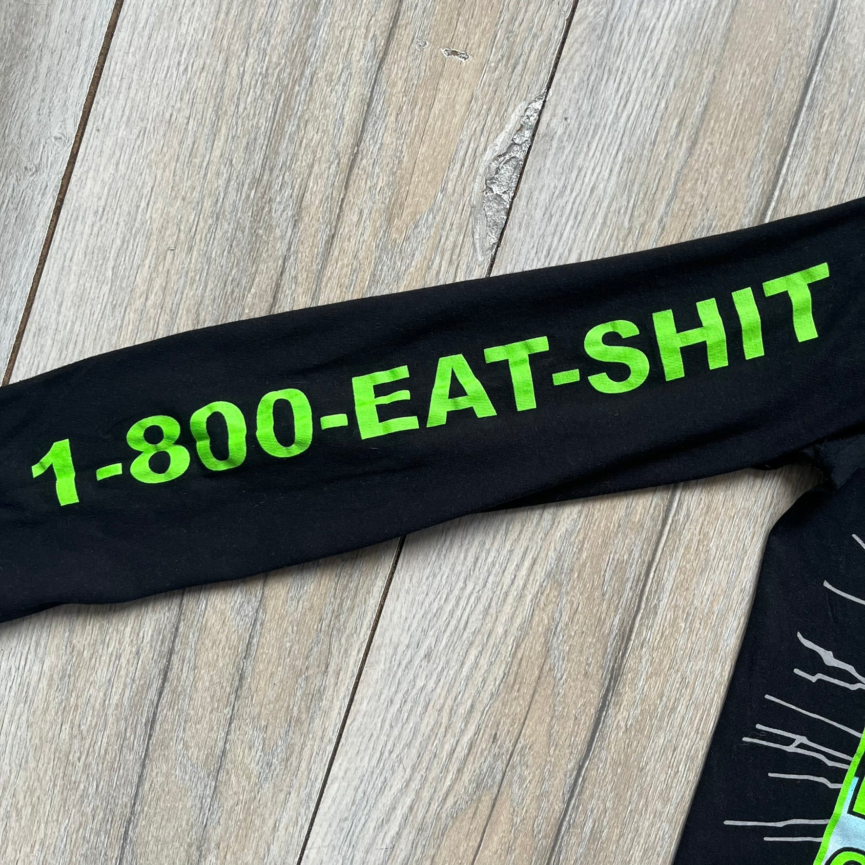 A$AP Rocky 2019 “Injured Generation” Tour “Pickpockets” Longsleeve is a black long-sleeve T-shirt released as part of the Injured Generation tour merchandise collection. The front features a large graphic of A$AP Rocky with green “Warning! Beware of Pickpockets” text. One sleeve includes “1-800-EAT-SHIT” text, while the other features a yellow and green testing-style logo. The back displays large green “Don’t Be a Dummy A$AP Rocky Europe” text layered over a white dummy mask graphic. Made in the USA.