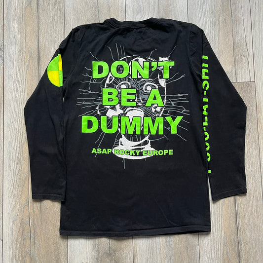 A$AP Rocky 2019 “Injured Generation” Tour “Pickpockets” Longsleeve is a black long-sleeve T-shirt released as part of the Injured Generation tour merchandise collection. The front features a large graphic of A$AP Rocky with green “Warning! Beware of Pickpockets” text. One sleeve includes “1-800-EAT-SHIT” text, while the other features a yellow and green testing-style logo. The back displays large green “Don’t Be a Dummy A$AP Rocky Europe” text layered over a white dummy mask graphic. Made in the USA.
