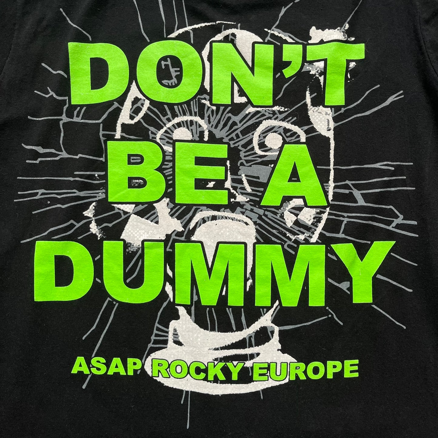 A$AP Rocky 2019 “Injured Generation” Tour “Pickpockets” Longsleeve is a black long-sleeve T-shirt released as part of the Injured Generation tour merchandise collection. The front features a large graphic of A$AP Rocky with green “Warning! Beware of Pickpockets” text. One sleeve includes “1-800-EAT-SHIT” text, while the other features a yellow and green testing-style logo. The back displays large green “Don’t Be a Dummy A$AP Rocky Europe” text layered over a white dummy mask graphic. Made in the USA.