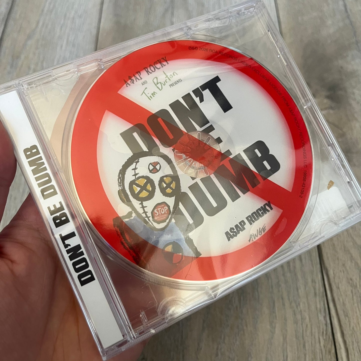 A$AP Rocky “Don’t Be Dumb” GRIM CD is a jewel case CD release of Don’t Be Dumb by A$AP Rocky featuring DUMMY artwork by Tim Burton. The cover includes large “Don’t Be Dumb” text with smaller “A$AP Rocky” and “Tim Burton Presents” above, along with the Dummy figure in a Dummy mask. The case spine features “Don’t Be Dumb” text, and the disc includes a foil design with a red crossed-out circle graphic.