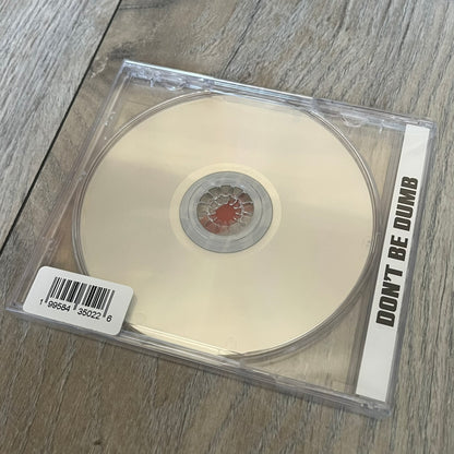A$AP Rocky “Don’t Be Dumb” GRIM CD is a jewel case CD release of Don’t Be Dumb by A$AP Rocky featuring DUMMY artwork by Tim Burton. The cover includes large “Don’t Be Dumb” text with smaller “A$AP Rocky” and “Tim Burton Presents” above, along with the Dummy figure in a Dummy mask. The case spine features “Don’t Be Dumb” text, and the disc includes a foil design with a red crossed-out circle graphic.