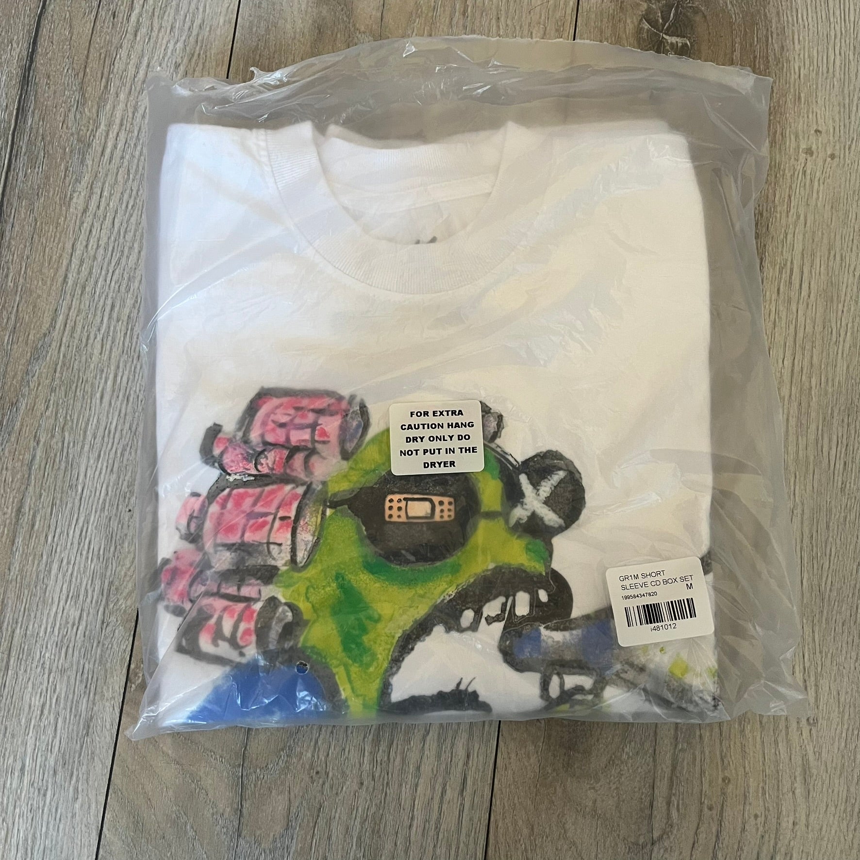 A$AP Rocky “Don’t Be Dumb” GR1M Short Sleeve Tee is a limited release from the AWGE website tied to the rollout of Don’t Be Dumb by A$AP Rocky. The white T-shirt features a green GR1M figure with a megaphone printed on the front with “GRIM” text below. The reverse includes a framed graphic with “Don’t Be Dumb” text, using a lenticular-style vinyl panel that shifts between the GR1M figure and A$AP Rocky in the same pose.