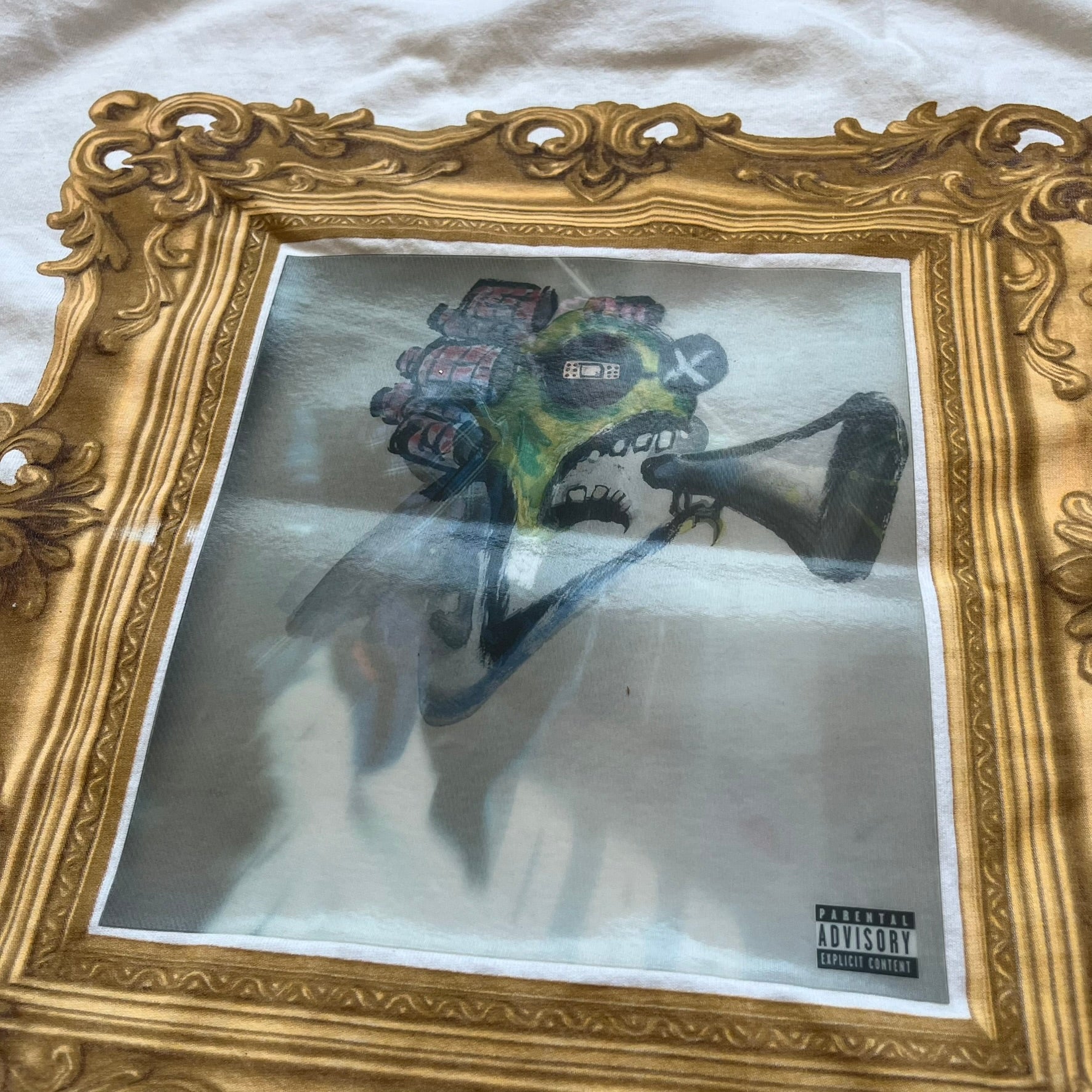 A$AP Rocky “Don’t Be Dumb” GR1M Short Sleeve Tee is a limited release from the AWGE website tied to the rollout of Don’t Be Dumb by A$AP Rocky. The white T-shirt features a green GR1M figure with a megaphone printed on the front with “GRIM” text below. The reverse includes a framed graphic with “Don’t Be Dumb” text, using a lenticular-style vinyl panel that shifts between the GR1M figure and A$AP Rocky in the same pose.