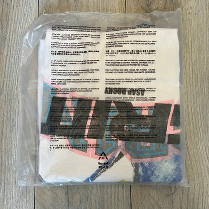A$AP Rocky “Don’t Be Dumb” GR1M Short Sleeve Tee is a limited release from the AWGE website tied to the rollout of Don’t Be Dumb by A$AP Rocky. The white T-shirt features a green GR1M figure with a megaphone printed on the front with “GRIM” text below. The reverse includes a framed graphic with “Don’t Be Dumb” text, using a lenticular-style vinyl panel that shifts between the GR1M figure and A$AP Rocky in the same pose.