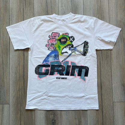 A$AP Rocky “Don’t Be Dumb” GR1M Short Sleeve Tee is a limited release from the AWGE website tied to the rollout of Don’t Be Dumb by A$AP Rocky. The white T-shirt features a green GR1M figure with a megaphone printed on the front with “GRIM” text below. The reverse includes a framed graphic with “Don’t Be Dumb” text, using a lenticular-style vinyl panel that shifts between the GR1M figure and A$AP Rocky in the same pose.