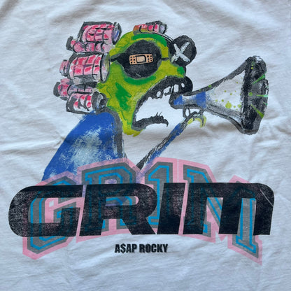 A$AP Rocky “Don’t Be Dumb” GR1M Short Sleeve Tee is a limited release from the AWGE website tied to the rollout of Don’t Be Dumb by A$AP Rocky. The white T-shirt features a green GR1M figure with a megaphone printed on the front with “GRIM” text below. The reverse includes a framed graphic with “Don’t Be Dumb” text, using a lenticular-style vinyl panel that shifts between the GR1M figure and A$AP Rocky in the same pose.
