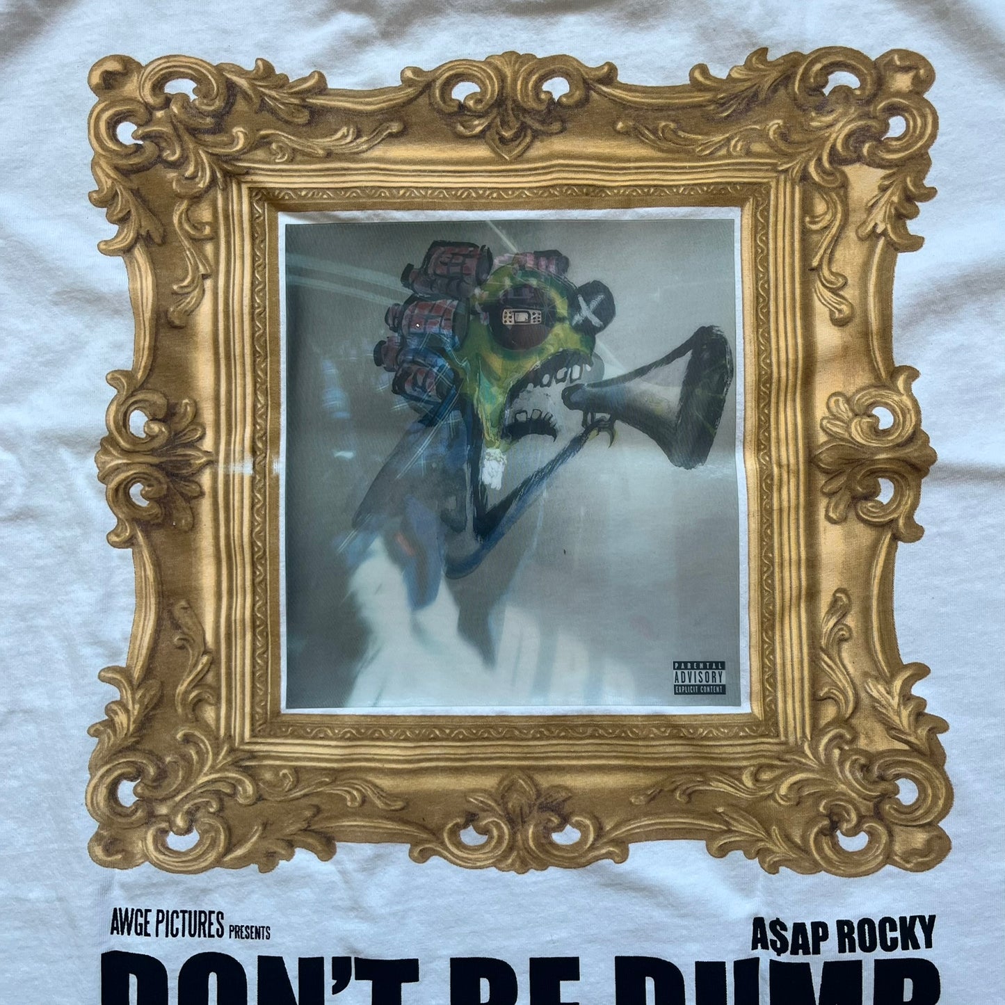 A$AP Rocky “Don’t Be Dumb” GR1M Short Sleeve Tee is a limited release from the AWGE website tied to the rollout of Don’t Be Dumb by A$AP Rocky. The white T-shirt features a green GR1M figure with a megaphone printed on the front with “GRIM” text below. The reverse includes a framed graphic with “Don’t Be Dumb” text, using a lenticular-style vinyl panel that shifts between the GR1M figure and A$AP Rocky in the same pose.