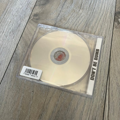 A$AP Rocky “Don’t Be Dumb” GRIM CD is a jewel case CD release of Don’t Be Dumb by A$AP Rocky featuring Mr. Mayers artwork by Tim Burton. The cover includes large “Don’t Be Dumb” text with smaller “A$AP Rocky” and “Tim Burton Presents” above, along with the Mr. Mayers figure in a blue trench coat. The case spine features “Don’t Be Dumb” text, and the disc includes a foil design with a red crossed-out circle graphic.