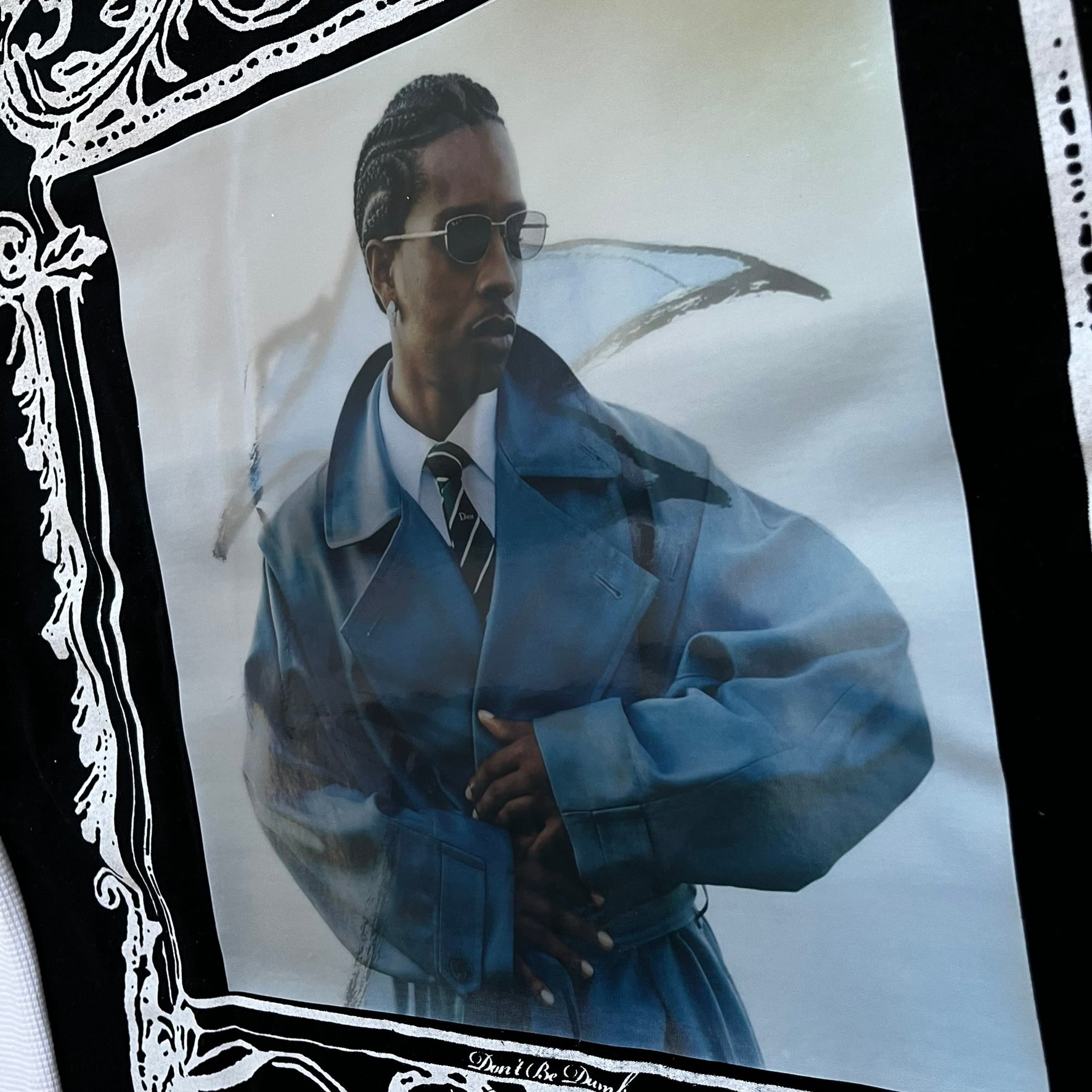 A$AP Rocky “Don’t Be Dumb” Mr Mayers Twofer Longsleeve is a limited release from the AWGE website tied to the rollout of Don’t Be Dumb by A$AP Rocky. The piece features a twofer construction with a black body and white sleeves, with a front graphic of the Mr Mayers figure in a blue trench coat with “Mr Mayers” text and small AWGE logos. The back includes a framed graphic with “Don’t Be Dumb” text, using a lenticular-style vinyl panel that shifts between the Mr Mayers figure and A$AP Rocky in the same outfit