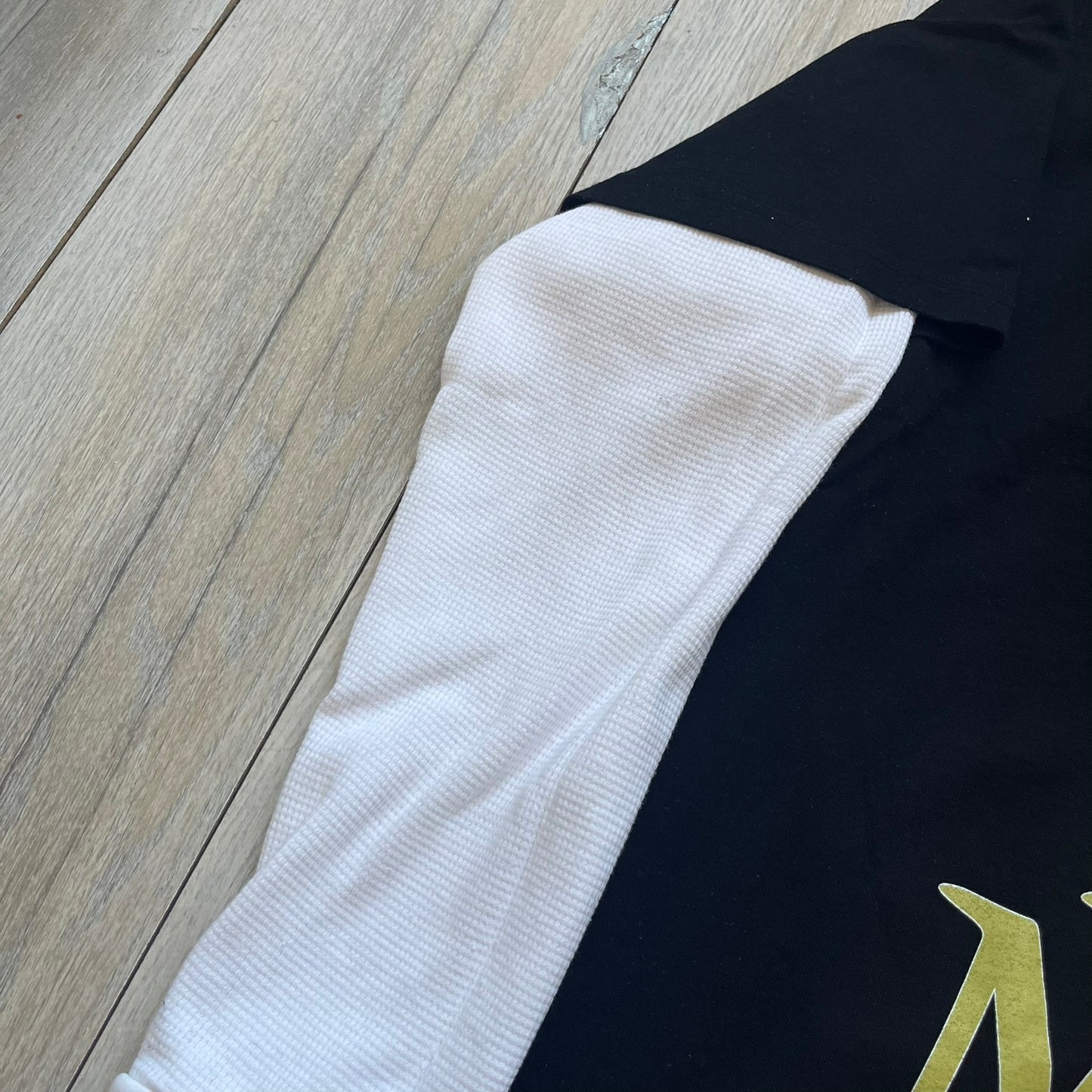 A$AP Rocky “Don’t Be Dumb” Mr Mayers Twofer Longsleeve is a limited release from the AWGE website tied to the rollout of Don’t Be Dumb by A$AP Rocky. The piece features a twofer construction with a black body and white sleeves, with a front graphic of the Mr Mayers figure in a blue trench coat with “Mr Mayers” text and small AWGE logos. The back includes a framed graphic with “Don’t Be Dumb” text, using a lenticular-style vinyl panel that shifts between the Mr Mayers figure and A$AP Rocky in the same outfit