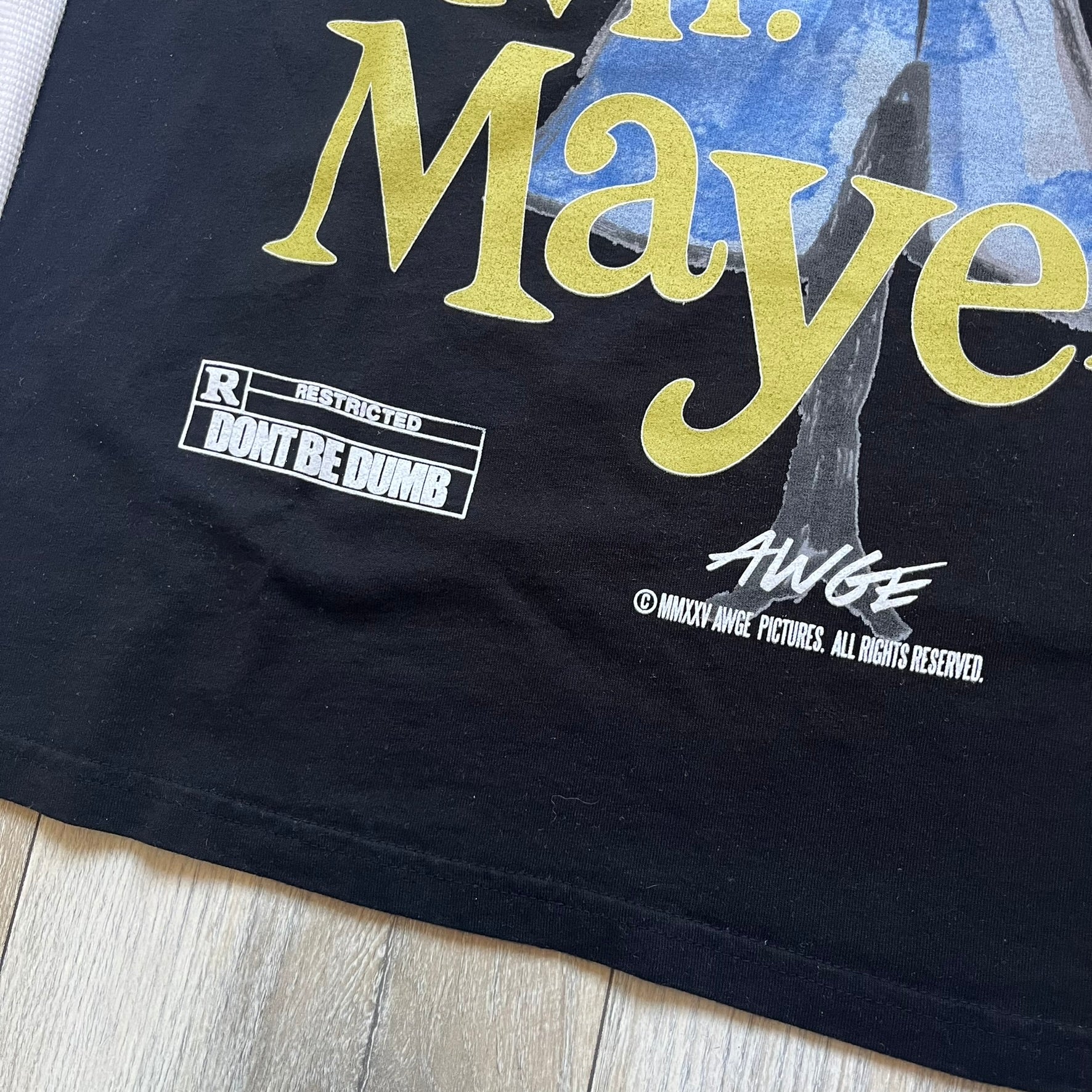 A$AP Rocky “Don’t Be Dumb” Mr Mayers Twofer Longsleeve is a limited release from the AWGE website tied to the rollout of Don’t Be Dumb by A$AP Rocky. The piece features a twofer construction with a black body and white sleeves, with a front graphic of the Mr Mayers figure in a blue trench coat with “Mr Mayers” text and small AWGE logos. The back includes a framed graphic with “Don’t Be Dumb” text, using a lenticular-style vinyl panel that shifts between the Mr Mayers figure and A$AP Rocky in the same outfit