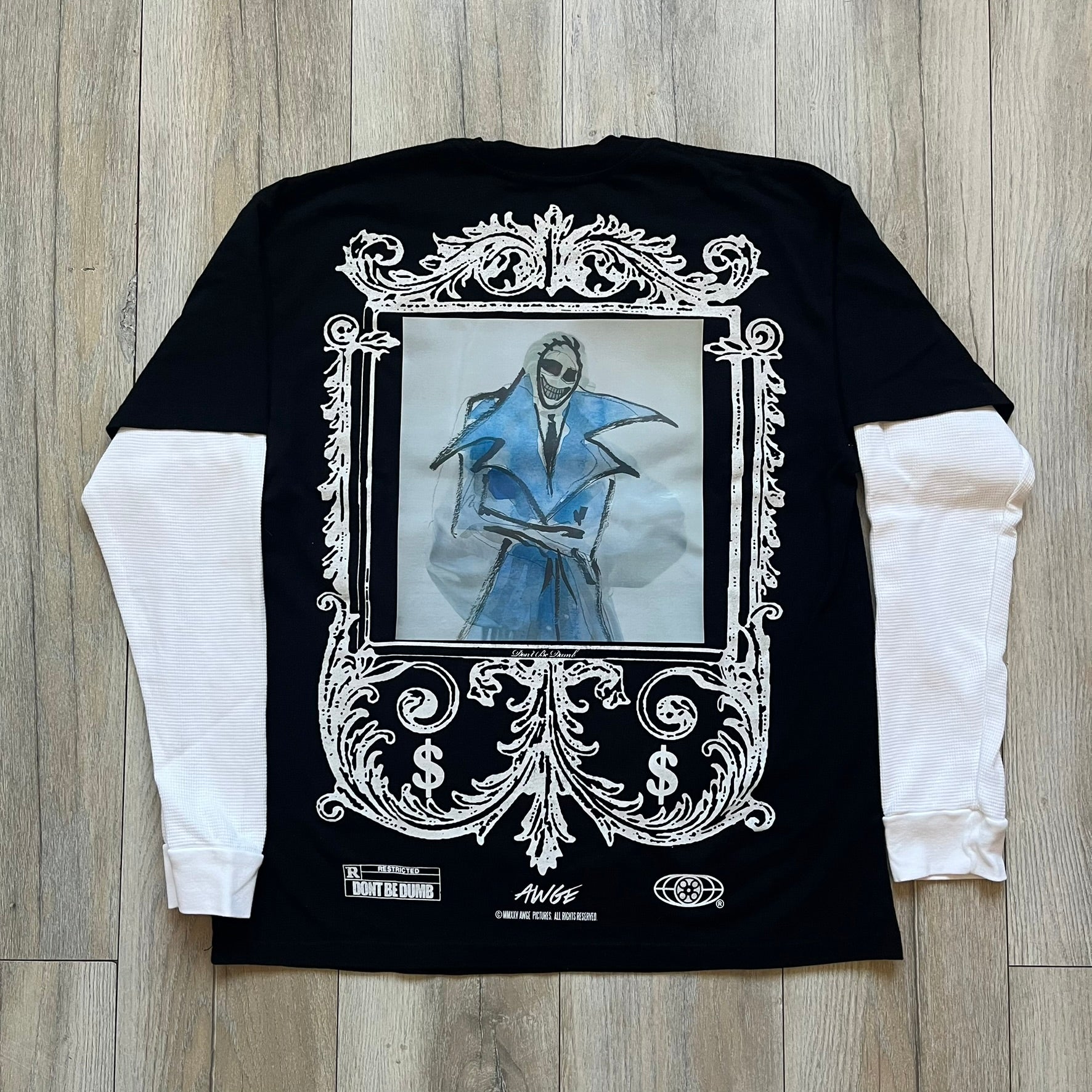 A$AP Rocky “Don’t Be Dumb” Mr Mayers Twofer Longsleeve is a limited release from the AWGE website tied to the rollout of Don’t Be Dumb by A$AP Rocky. The piece features a twofer construction with a black body and white sleeves, with a front graphic of the Mr Mayers figure in a blue trench coat with “Mr Mayers” text and small AWGE logos. The back includes a framed graphic with “Don’t Be Dumb” text, using a lenticular-style vinyl panel that shifts between the Mr Mayers figure and A$AP Rocky in the same outfit