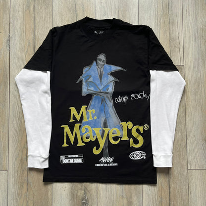 A$AP Rocky “Don’t Be Dumb” Mr Mayers Twofer Longsleeve is a limited release from the AWGE website tied to the rollout of Don’t Be Dumb by A$AP Rocky. The piece features a twofer construction with a black body and white sleeves, with a front graphic of the Mr Mayers figure in a blue trench coat with “Mr Mayers” text and small AWGE logos. The back includes a framed graphic with “Don’t Be Dumb” text, using a lenticular-style vinyl panel that shifts between the Mr Mayers figure and A$AP Rocky in the same outfit