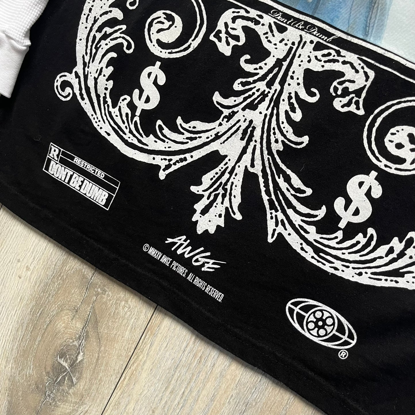 A$AP Rocky “Don’t Be Dumb” Mr Mayers Twofer Longsleeve is a limited release from the AWGE website tied to the rollout of Don’t Be Dumb by A$AP Rocky. The piece features a twofer construction with a black body and white sleeves, with a front graphic of the Mr Mayers figure in a blue trench coat with “Mr Mayers” text and small AWGE logos. The back includes a framed graphic with “Don’t Be Dumb” text, using a lenticular-style vinyl panel that shifts between the Mr Mayers figure and A$AP Rocky in the same outfit