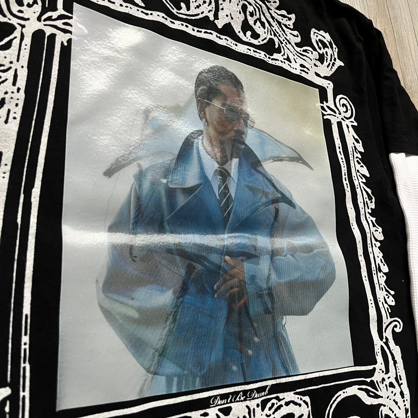 A$AP Rocky “Don’t Be Dumb” Mr Mayers Twofer Longsleeve is a limited release from the AWGE website tied to the rollout of Don’t Be Dumb by A$AP Rocky. The piece features a twofer construction with a black body and white sleeves, with a front graphic of the Mr Mayers figure in a blue trench coat with “Mr Mayers” text and small AWGE logos. The back includes a framed graphic with “Don’t Be Dumb” text, using a lenticular-style vinyl panel that shifts between the Mr Mayers figure and A$AP Rocky in the same outfit
