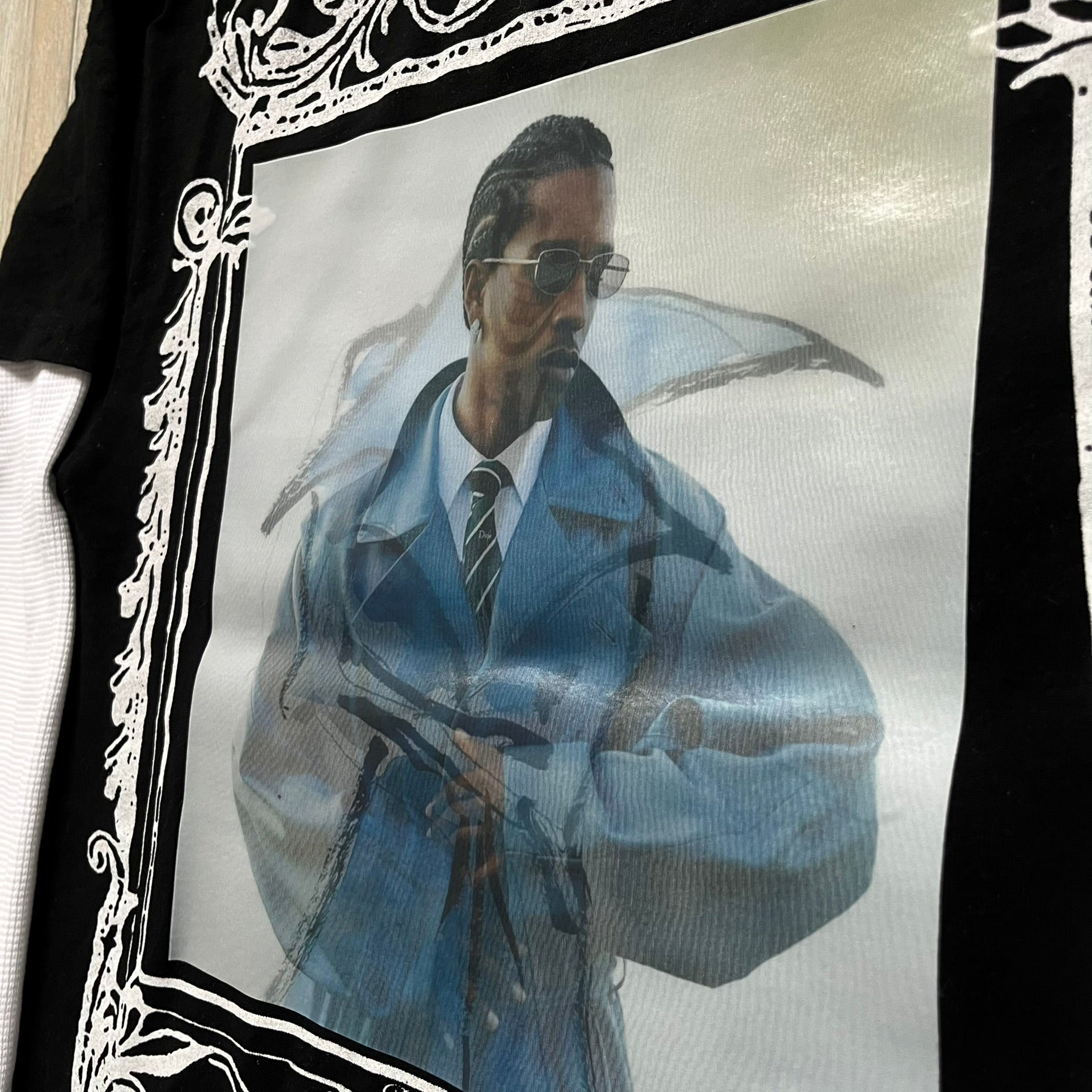 A$AP Rocky “Don’t Be Dumb” Mr Mayers Twofer Longsleeve is a limited release from the AWGE website tied to the rollout of Don’t Be Dumb by A$AP Rocky. The piece features a twofer construction with a black body and white sleeves, with a front graphic of the Mr Mayers figure in a blue trench coat with “Mr Mayers” text and small AWGE logos. The back includes a framed graphic with “Don’t Be Dumb” text, using a lenticular-style vinyl panel that shifts between the Mr Mayers figure and A$AP Rocky in the same outfit