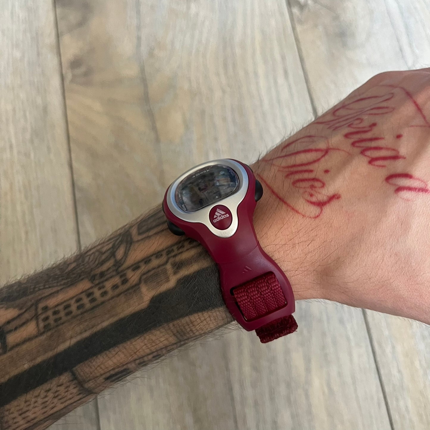 Adidas 2000s Burgundy 10-0117 Digital Watch (model X-003) is a burgundy digital watch with a silver bezel and ergonomic case. It features a burgundy nylon Velcro strap and four side buttons. The design includes three white stripes on the case and a silver Adidas logo button below the screen. The stainless steel back is engraved and marked water resistant up to 3 ATM, with an Adidas logo patch on the strap.