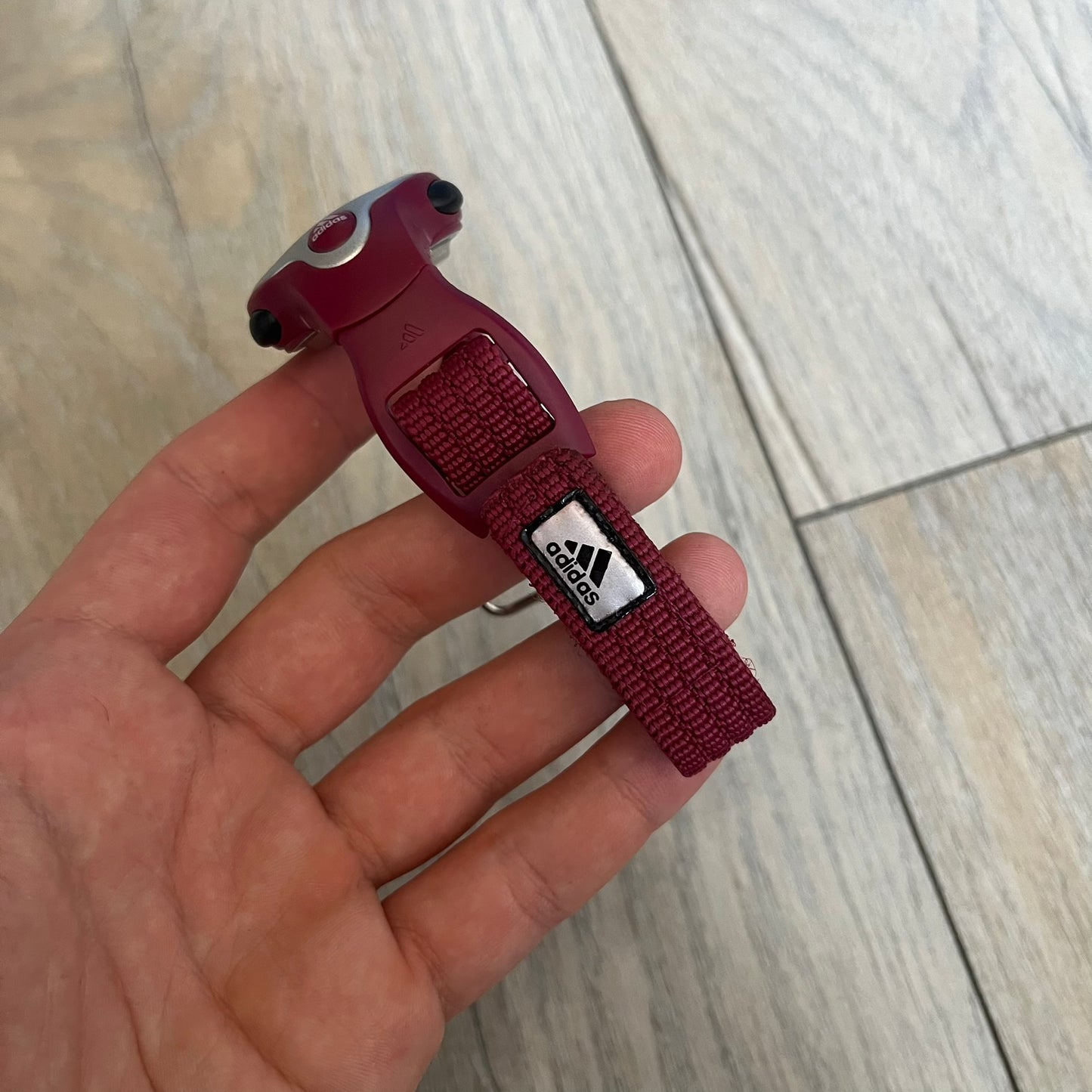 Adidas 2000s Burgundy 10-0117 Digital Watch (model X-003) is a burgundy digital watch with a silver bezel and ergonomic case. It features a burgundy nylon Velcro strap and four side buttons. The design includes three white stripes on the case and a silver Adidas logo button below the screen. The stainless steel back is engraved and marked water resistant up to 3 ATM, with an Adidas logo patch on the strap.