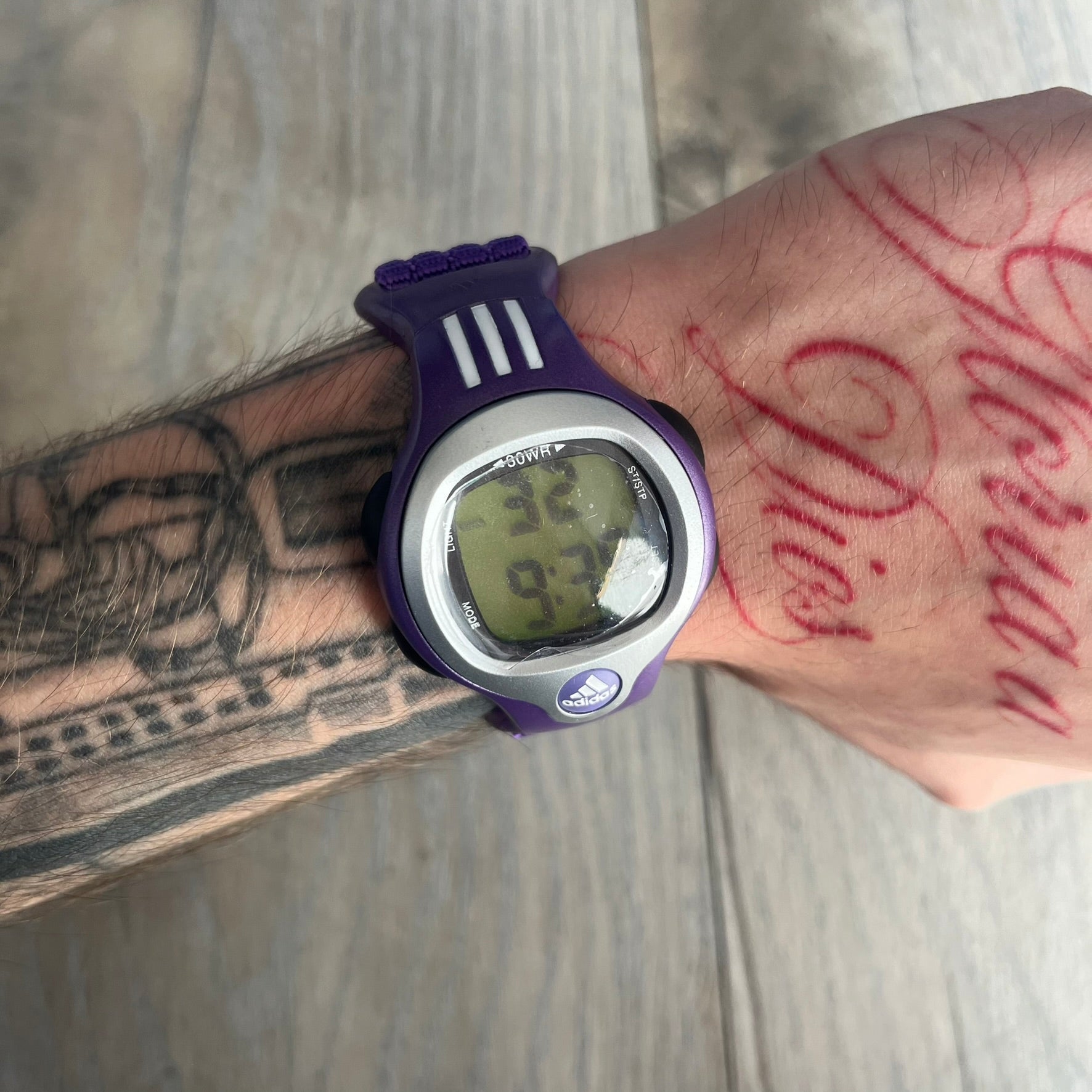 Adidas 2000s Purple 10-0117 Digital Watch (model X-003) is a purple digital watch with a silver bezel and ergonomic case. It features a purple nylon Velcro strap, four side buttons, and a blue-green backlight display showing Adidas logo. The design includes three white stripes on the case and a silver Adidas logo button below the screen. The stainless steel back is engraved and marked water resistant up to 3 ATM, with an Adidas logo patch on the strap.