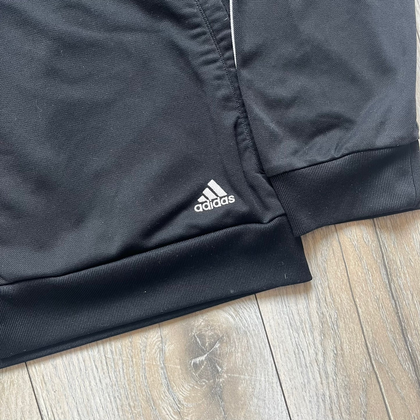 Adidas 2009 Doodle Track Jacket is a black track jacket with white Adidas stripes running down the sleeves. The upper chest area on both the front and back is covered in an all-over white doodle and graffiti-style print. It features a full zip closure and a small pocket on the left chest.
