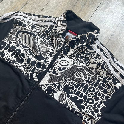 Adidas 2009 Doodle Track Jacket is a black track jacket with white Adidas stripes running down the sleeves. The upper chest area on both the front and back is covered in an all-over white doodle and graffiti-style print. It features a full zip closure and a small pocket on the left chest.
