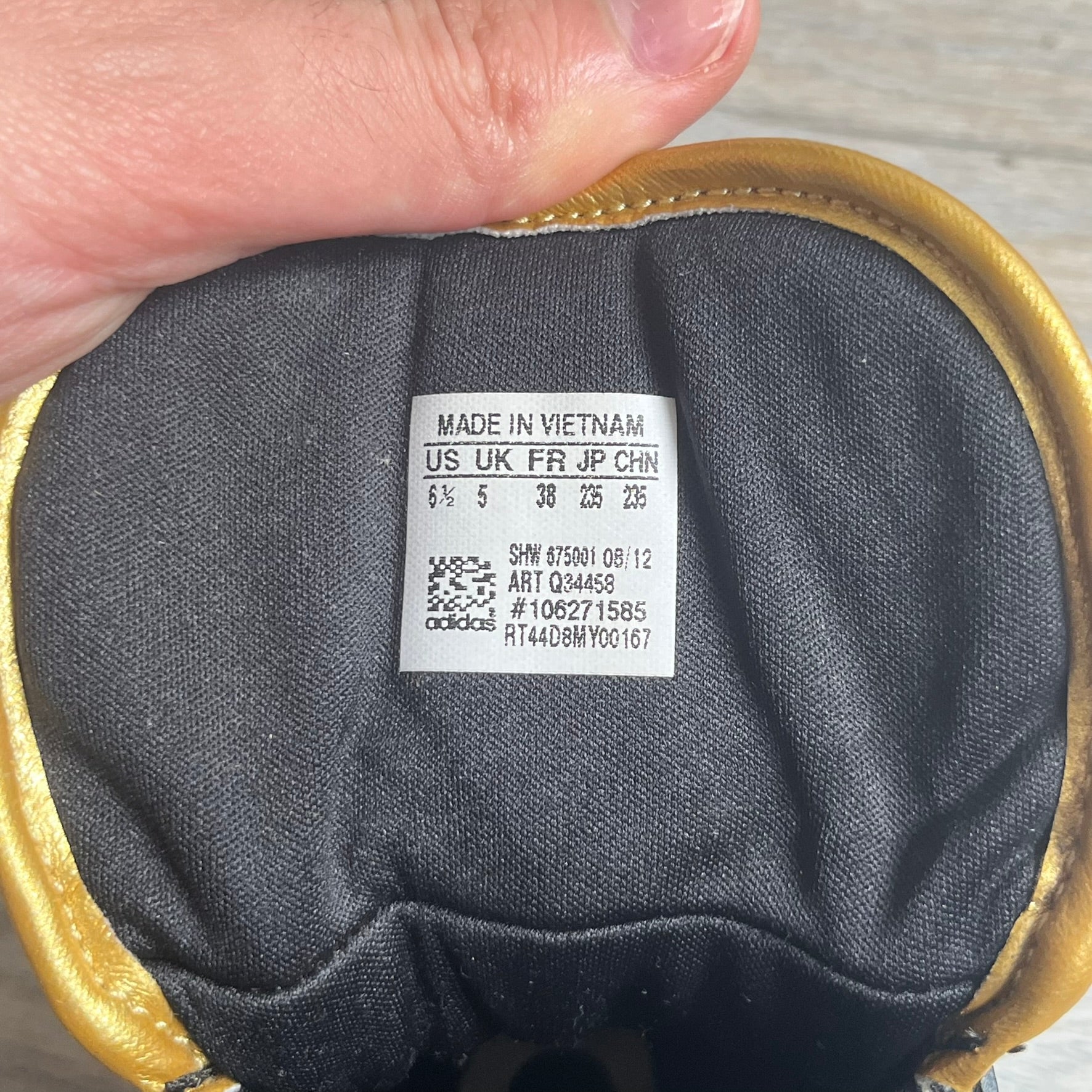 Adidas Space Diver Zip Pack Sneakers were released on November 18, 2012. The shoes feature a black upper with a glossy leather-like finish, gold detailing, and a white outsole and insole. The tongue has a large gold Trefoil logo with a gold outline, while the heel strap is printed with gold Adidas text. The sides feature three gold stripes designed as decorative zipper elements. A small white Adidas logo is also present on the upper.