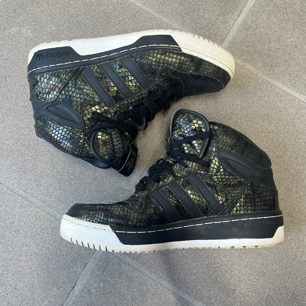 Adidas 2016 M Attitude Revive Snakeskin Sneakers are dark green sneakers covered in a shiny snakeskin-textured material, featuring black side stripes and a dark green Adidas Trefoil logo on the tongue. The sole is white with black accents.