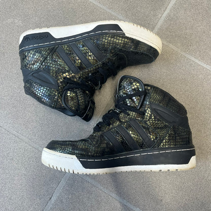 Adidas 2016 M Attitude Revive Snakeskin Sneakers are dark green sneakers covered in a shiny snakeskin-textured material, featuring black side stripes and a dark green Adidas Trefoil logo on the tongue. The sole is white with black accents.