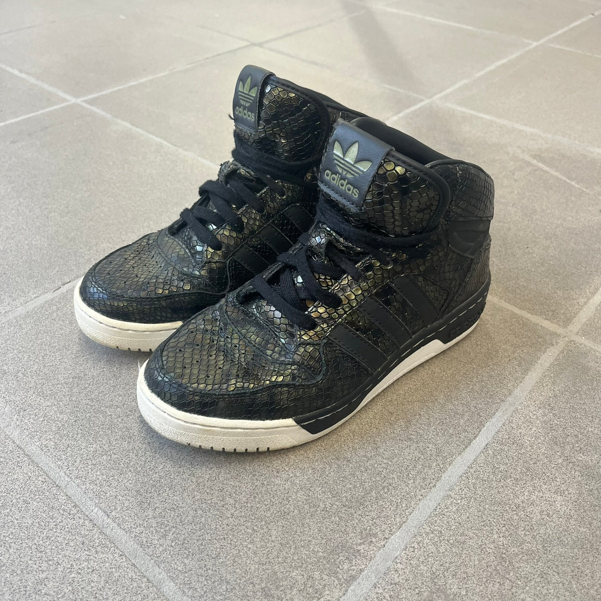 Adidas 2016 M Attitude Revive Snakeskin Sneakers are dark green sneakers covered in a shiny snakeskin-textured material, featuring black side stripes and a dark green Adidas Trefoil logo on the tongue. The sole is white with black accents.