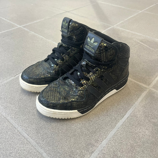 Adidas 2016 M Attitude Revive Snakeskin Sneakers are dark green sneakers covered in a shiny snakeskin-textured material, featuring black side stripes and a dark green Adidas Trefoil logo on the tongue. The sole is white with black accents.