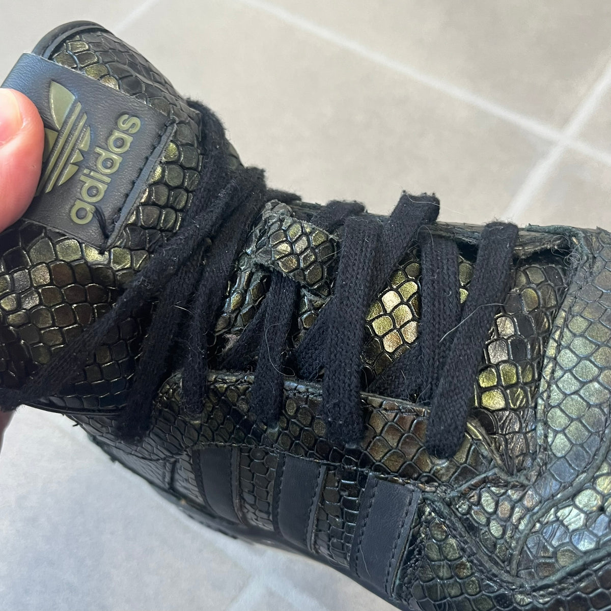 Adidas 2016 M Attitude Revive Snakeskin Sneakers are dark green sneakers covered in a shiny snakeskin-textured material, featuring black side stripes and a dark green Adidas Trefoil logo on the tongue. The sole is white with black accents.