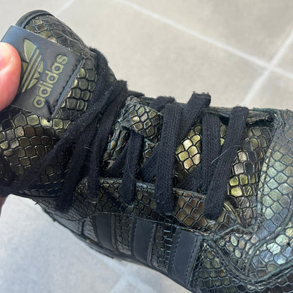 Adidas 2016 M Attitude Revive Snakeskin Sneakers are dark green sneakers covered in a shiny snakeskin-textured material, featuring black side stripes and a dark green Adidas Trefoil logo on the tongue. The sole is white with black accents.