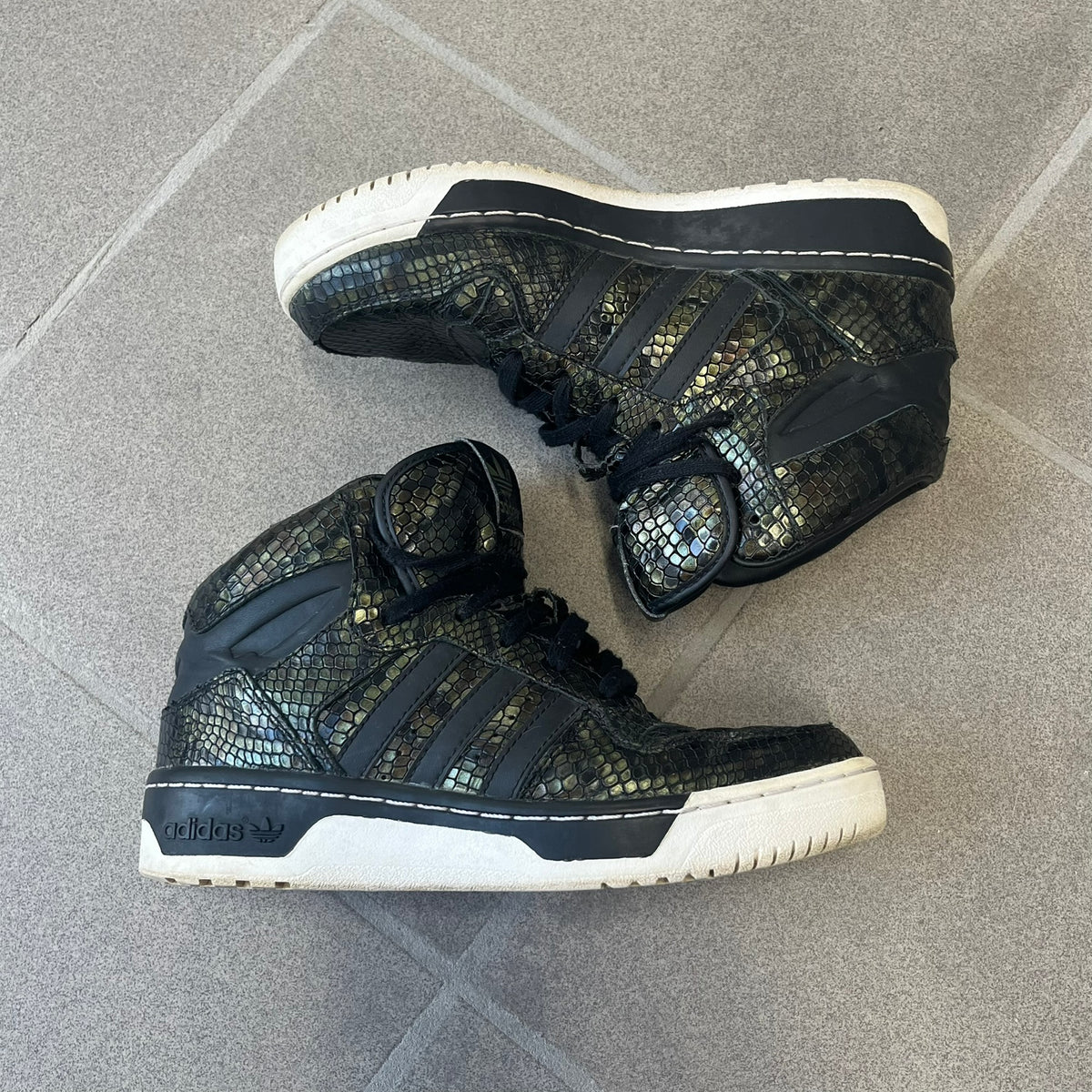 Adidas 2016 M Attitude Revive Snakeskin Sneakers are dark green sneakers covered in a shiny snakeskin-textured material, featuring black side stripes and a dark green Adidas Trefoil logo on the tongue. The sole is white with black accents.