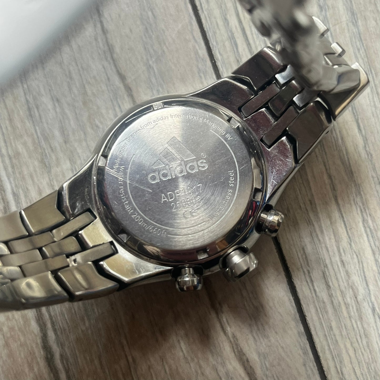 Adidas Adi-Star Pro Chrono ADP-1017 Analog Watch is a stainless steel timepiece with a white dial featuring the Adidas logo and three subdials for chronograph functions. It has two side buttons and a crown for adjustments, with a detailed and textured dial design. The watch is water resistant up to 200 meters.