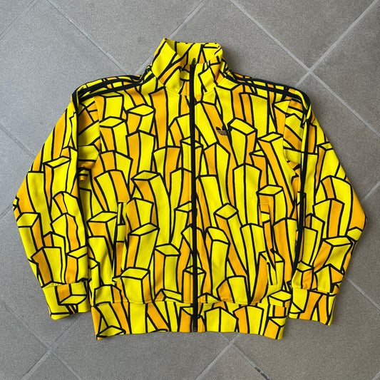 Adidas Originals x Jeremy Scott 2010 French Fry Track Jacket features an all-over yellow and black cartoon French fries print. The jacket is detailed with black Three Stripes along the sleeves, a small embroidered Trefoil logo on the chest, and a large black Trefoil with Adidas text printed across the back.