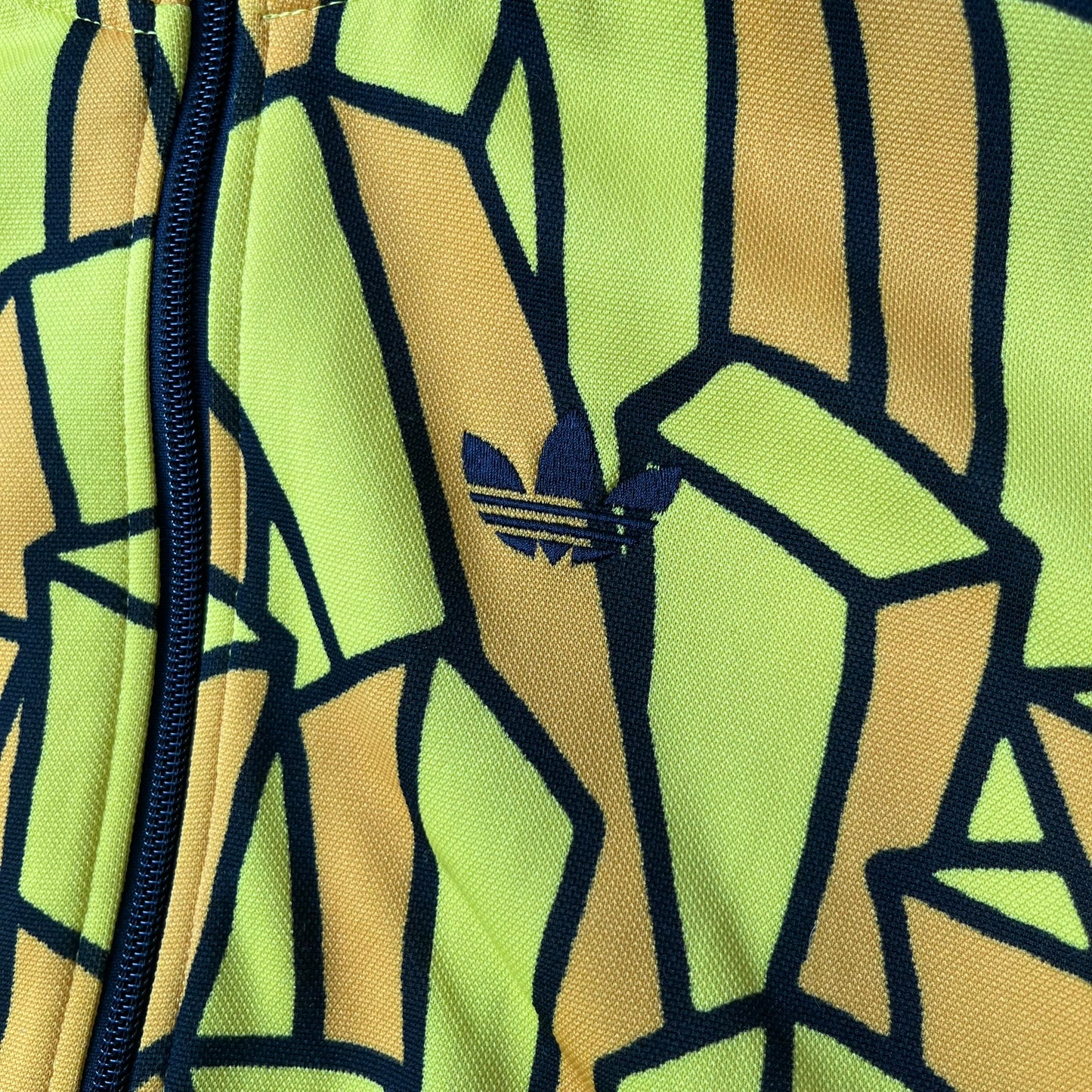 Adidas Originals x Jeremy Scott 2010 French Fry Track Jacket features an all-over yellow and black cartoon French fries print. The jacket is detailed with black Three Stripes along the sleeves, a small embroidered Trefoil logo on the chest, and a large black Trefoil with Adidas text printed across the back.