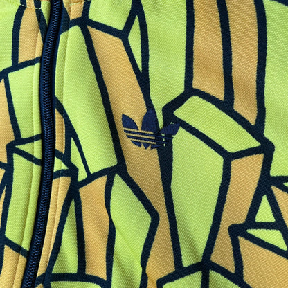 Adidas Originals x Jeremy Scott 2010 French Fry Track Jacket features an all-over yellow and black cartoon French fries print. The jacket is detailed with black Three Stripes along the sleeves, a small embroidered Trefoil logo on the chest, and a large black Trefoil with Adidas text printed across the back.