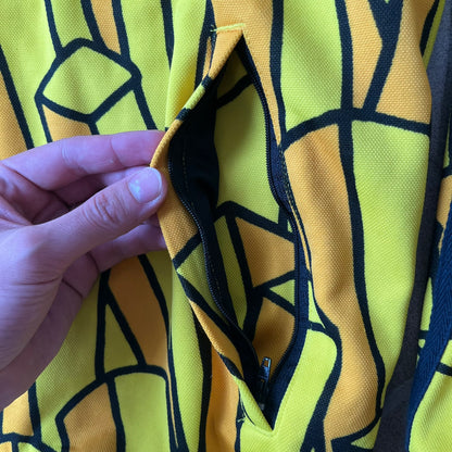 Adidas Originals x Jeremy Scott 2010 French Fry Track Jacket features an all-over yellow and black cartoon French fries print. The jacket is detailed with black Three Stripes along the sleeves, a small embroidered Trefoil logo on the chest, and a large black Trefoil with Adidas text printed across the back.