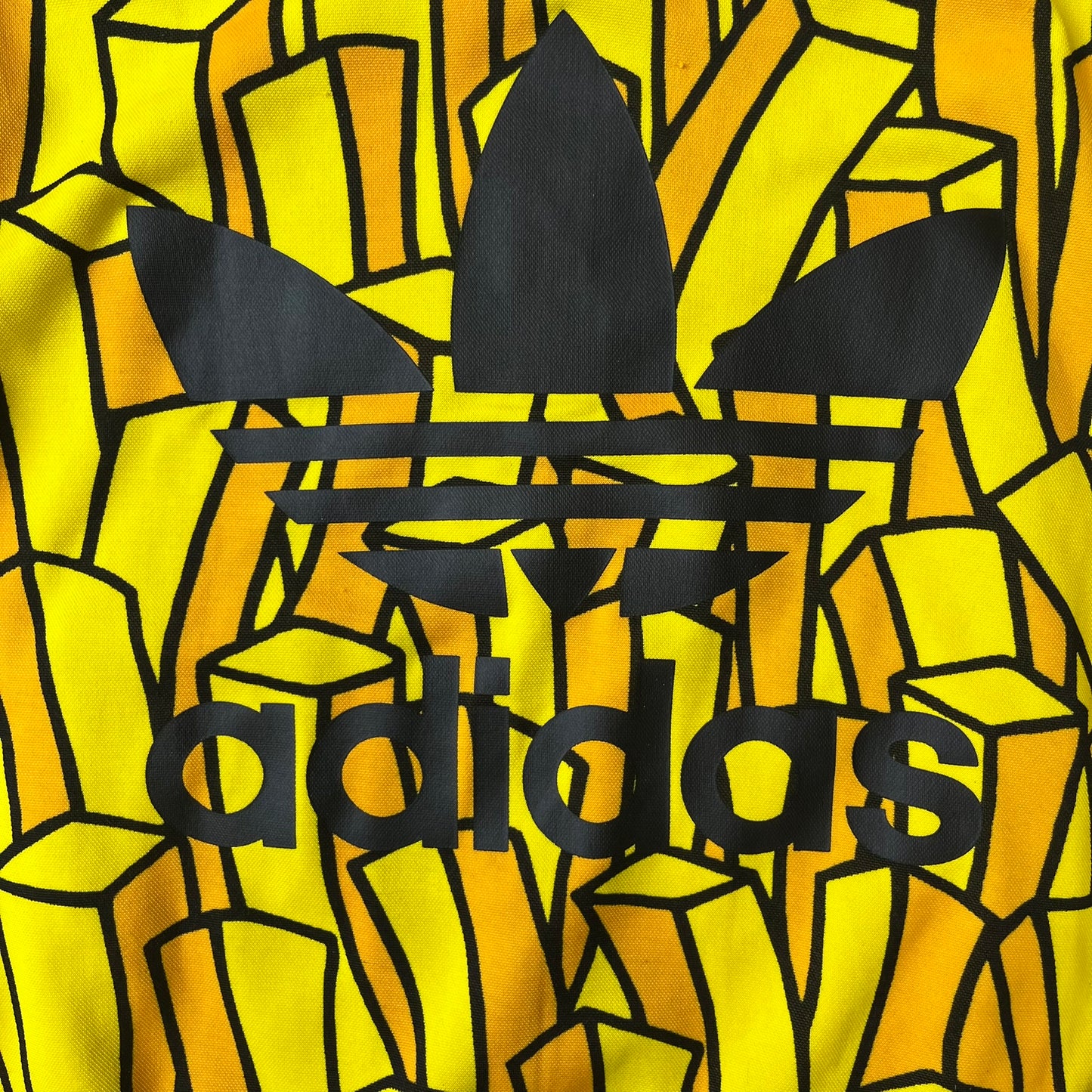 Adidas Originals x Jeremy Scott 2010 French Fry Track Jacket features an all-over yellow and black cartoon French fries print. The jacket is detailed with black Three Stripes along the sleeves, a small embroidered Trefoil logo on the chest, and a large black Trefoil with Adidas text printed across the back.