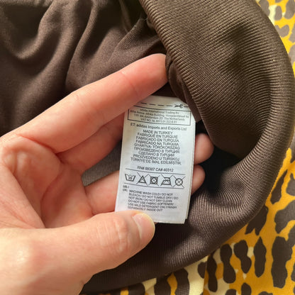 Adidas x Jeremy Scott 2015 Leopard Sequin Track Jacket features an all-over orange, brown, and white leopard print pattern with brown hems throughout. The jacket includes brown Adidas three-stripe detailing on the shoulders and sleeves, zippered front pockets, and multicolor embroidered sequin “adi” and “das” chest branding in Jeremy Scott styling. The back is finished with a large embroidered sequin Adidas Trefoil logo, and the piece comes with original paper tag.