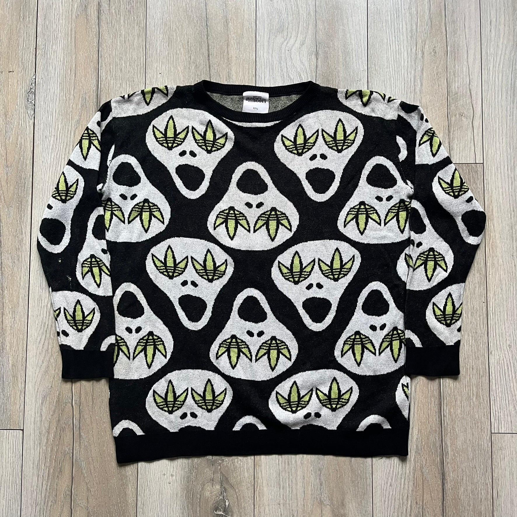 Adidas Jeremy Scott Alien Face 2012 Sweater features an all-over print of white alien faces arranged in alternating upright and upside-down patterns. The eyes of each alien are replaced with green Adidas Originals logos, creating a distinctive graphic design.