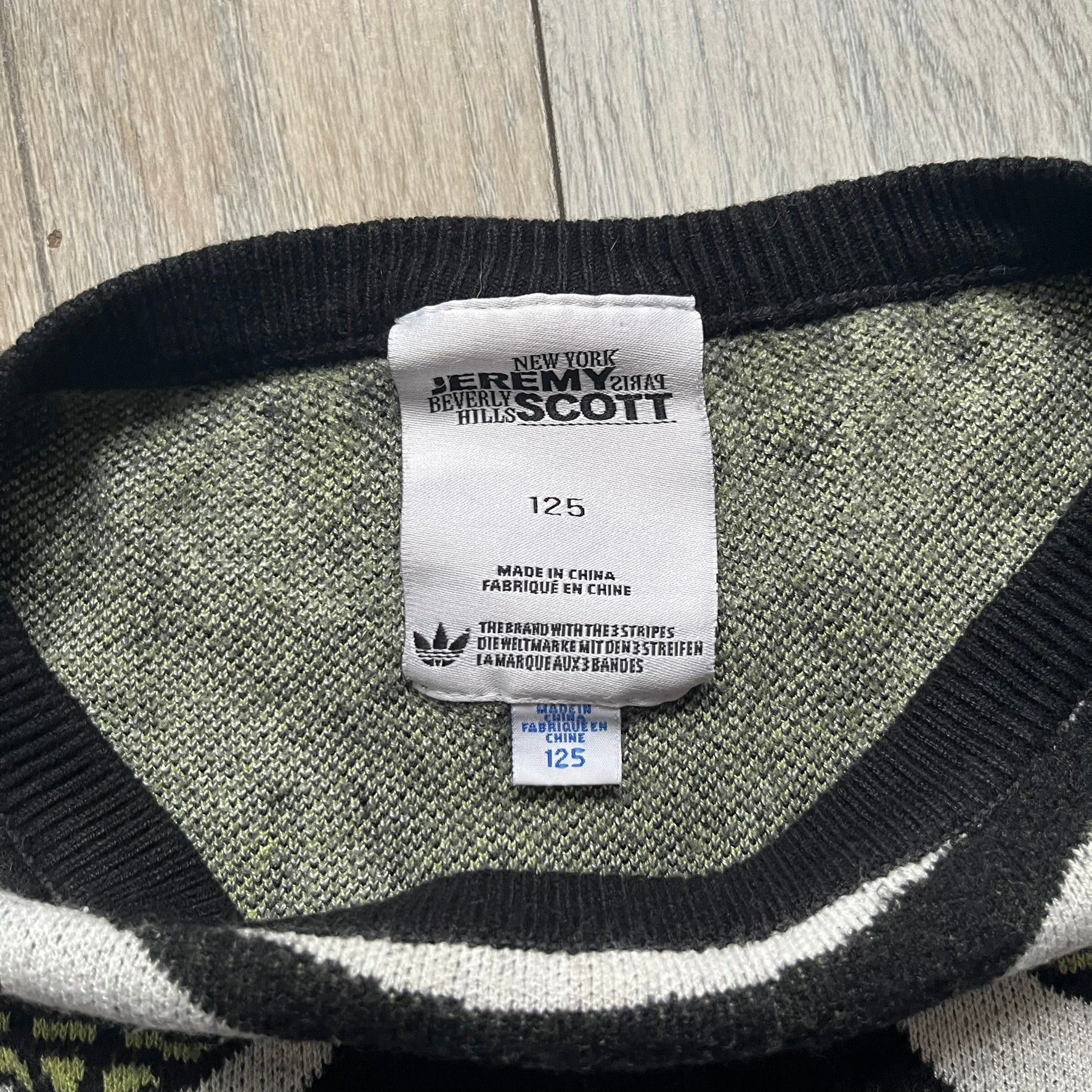 Adidas Jeremy Scott Alien Face 2012 Sweater features an all-over print of white alien faces arranged in alternating upright and upside-down patterns. The eyes of each alien are replaced with green Adidas Originals logos, creating a distinctive graphic design.