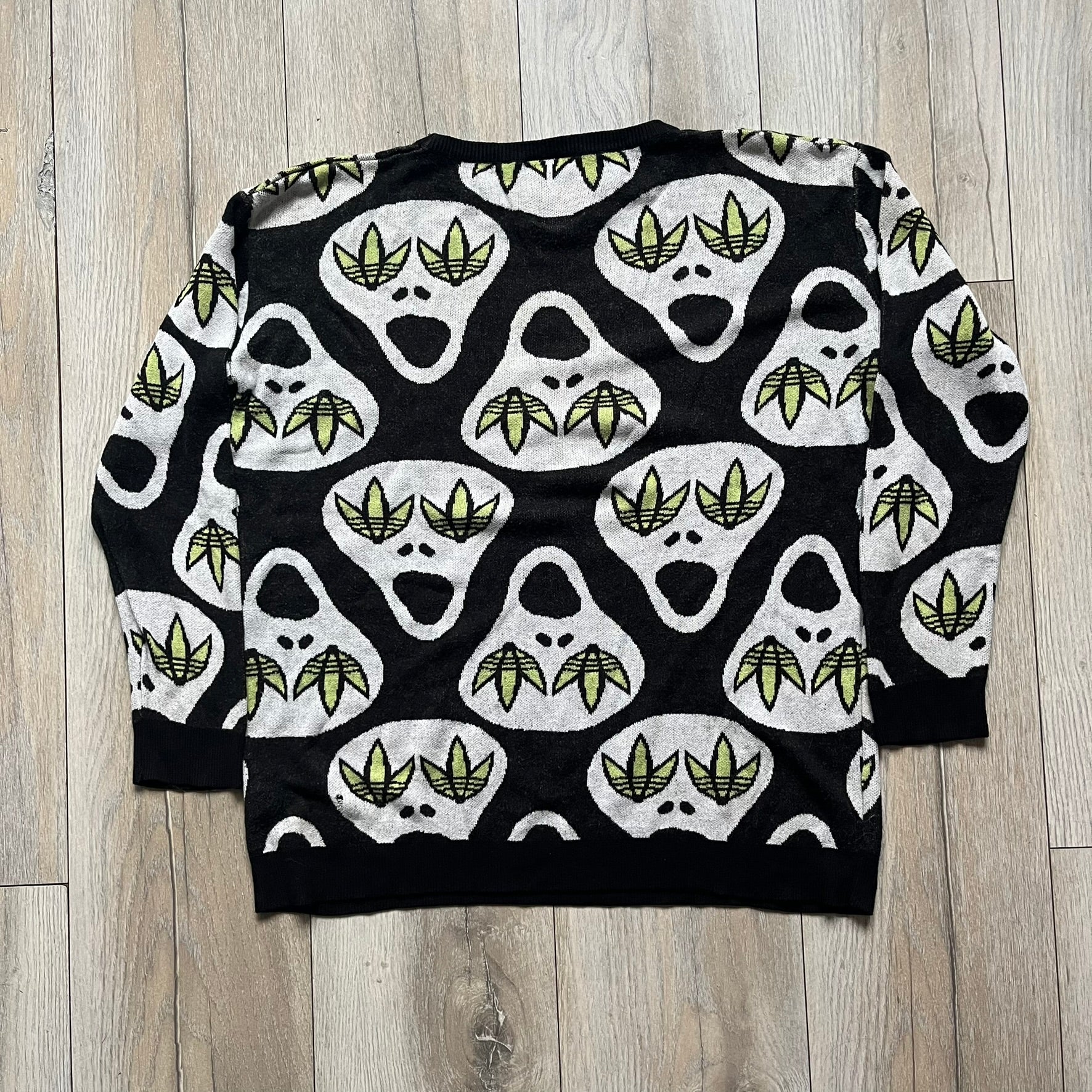 Adidas Jeremy Scott Alien Face 2012 Sweater features an all-over print of white alien faces arranged in alternating upright and upside-down patterns. The eyes of each alien are replaced with green Adidas Originals logos, creating a distinctive graphic design.