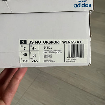 The Adidas Jeremy Scott Motorsport Wings 4.0 features a leather upper in blue with a gradient transitioning to green, accented by shock pink and light pink logo stripes. This high-top sneaker includes breathable perforations, a grippy rubber outsole, padded tongue, and signature Wings detailing at the collar. Released in 2022, the limited edition model comes with its original box and is crafted for comfort and style.