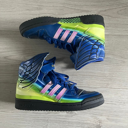 The Adidas Jeremy Scott Motorsport Wings 4.0 features a leather upper in blue with a gradient transitioning to green, accented by shock pink and light pink logo stripes. This high-top sneaker includes breathable perforations, a grippy rubber outsole, padded tongue, and signature Wings detailing at the collar. Released in 2022, the limited edition model comes with its original box and is crafted for comfort and style.